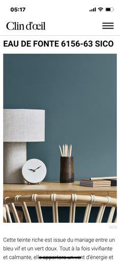 a table with a clock on it next to a lamp and some books in front of a blue wall