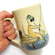 a hand holding a coffee mug with a drawing of a man fishing