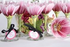 there are many wine glasses with pink flowers in them and labels on the glass vases