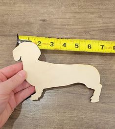 a hand holding a wooden cutout of a dog next to a measuring tape on a table