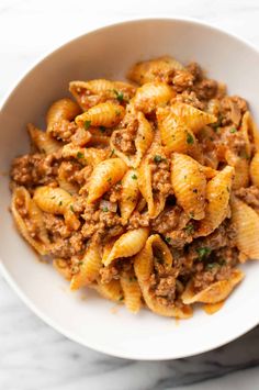 a white bowl filled with pasta covered in ground beef and sauce on top of a marble table