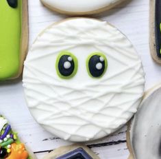 decorated cookies with green eyes and white icing are on a table next to candy