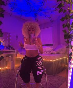 a woman sitting on a stool taking a selfie with her cell phone in a purple lit room