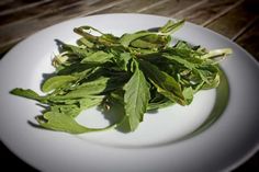 a white plate topped with greens on top of a wooden table