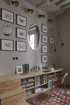 a room with many framed pictures on the wall and a desk in front of it