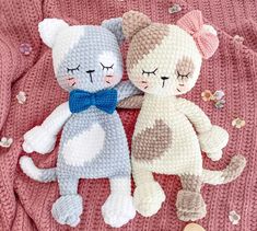 two knitted cats laying next to each other on top of a pink blanket with buttons