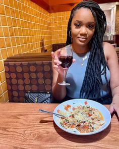 a woman sitting at a table with a plate of food and a glass of wine