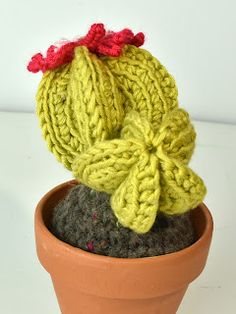 a crocheted cactus in a clay pot with a red flower on its head