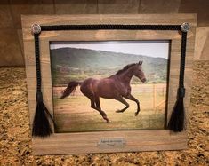 a horse running through a field in a wooden frame on a granite counter top with a mountain behind it