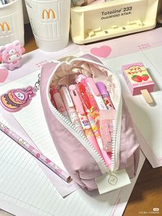 the contents of a pink purse sitting on top of a desk next to some pens and pencils