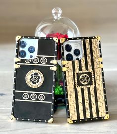 two black and gold cell phones sitting next to each other on a table with flowers