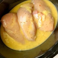 two pieces of chicken in a sauce in a black crock pot on a white table