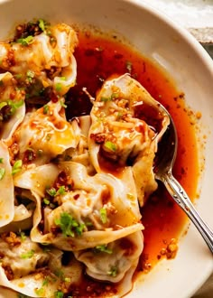 a white bowl filled with dumplings covered in sauce and garnished with green onions