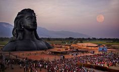 a large group of people standing in front of a giant buddha statue at dusk with the moon behind it