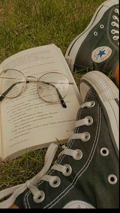 an open book and pair of glasses sitting on the grass with their feet propped up