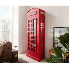 a red phone booth sitting in front of a window next to a couch and potted plant