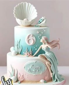 a birthday cake with a mermaid on top and seashells in the background,