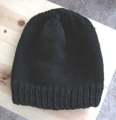 a black knitted beanie sitting on top of a wooden table next to a piece of wood