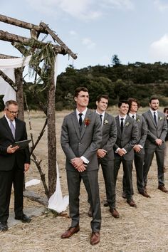 a group of men standing next to each other in front of a wooden structure on top of a field