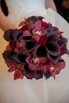 the bride's bouquet is made up of red and black orchids, which are accented with purple calla lilies