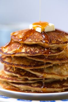 a stack of pancakes with syrup and butter being drizzled over them on a blue and white plate