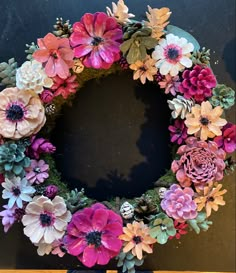 a wreath made out of fake flowers sitting on top of a wooden table in front of a black wall