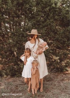 a woman and two children standing in front of some trees with their arms around each other