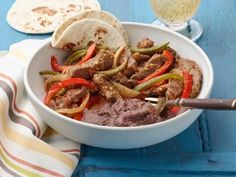 a white bowl filled with meat and vegetables next to tortilla bread on top of a blue table