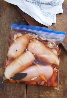 a bag of chicken and carrots sitting on top of a wooden table next to a knife