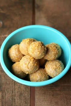 a blue bowl filled with doughnut holes on top of a wooden table next to a cup of coffee