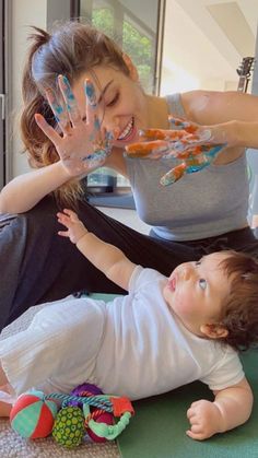 a woman sitting on the floor with her baby and hands painted in blue and orange