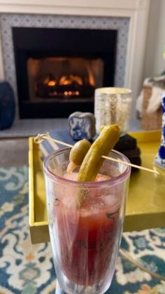 a drink with pickles in it sitting on a table next to a fire place