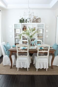 a dining room table with white chairs and blue pillows