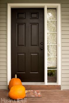 two pumpkins sitting on the front steps of a house with a black door and window