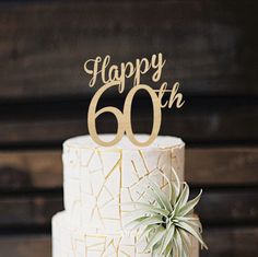 a white cake with gold letters and a succulent decoration on top that says happy 60th