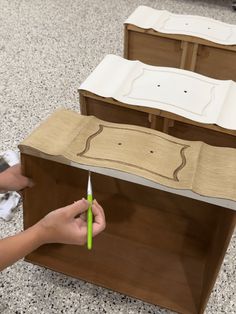 a person is using scissors to cut out the top of a wooden cabinet with drawers