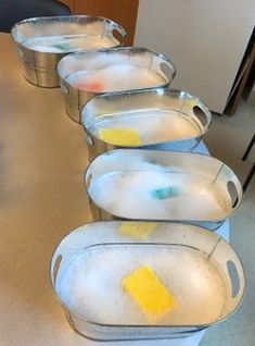 five metal pans are lined up on the table with yellow and blue paint in them