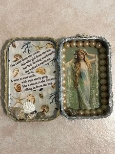 an open tin box with pearls and beads on the inside that has a picture of a mermaid in it