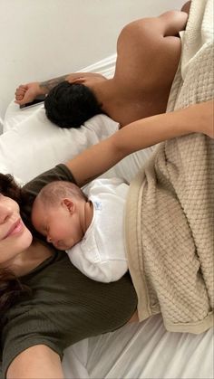 a woman laying on top of a bed next to a baby