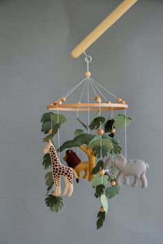 a mobile with animals hanging from it's sides and leaves on the bottom, in front of a gray wall