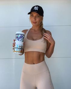 a woman is holding a drink and posing for the camera while wearing her sports bra