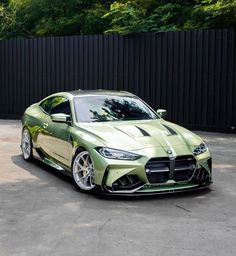 a green sports car parked in front of a black fence with trees and bushes behind it