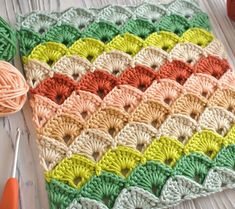 a crocheted granny blanket sitting on top of a wooden table next to yarn