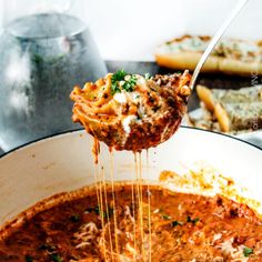 a ladle full of spaghetti being lifted from a pot filled with meat and cheese