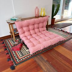 a pink futon chair sitting on top of a wooden floor next to a rug