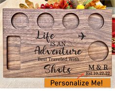 a wooden plaque with the words life is an adventure and shots on it, surrounded by fall leaves