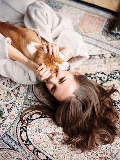 a woman laying on top of a rug holding a brown and white dog in her hands