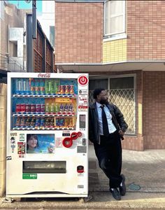 a man standing next to a vending machine on the side of a road in front of a building