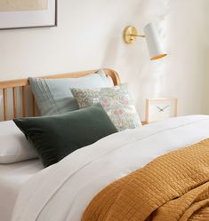 a bed with pillows and blankets on it next to a wall lamp in a bedroom