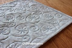 a close up of a rug on a wooden floor with the words quiltfabrication written across it